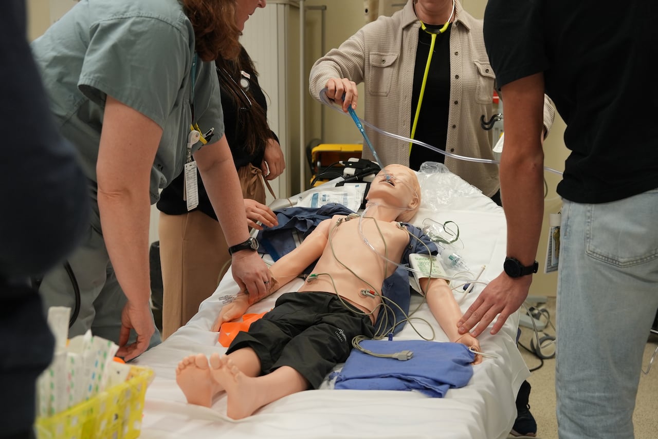 Medical staff gathered around a mannequin hooked up to machines