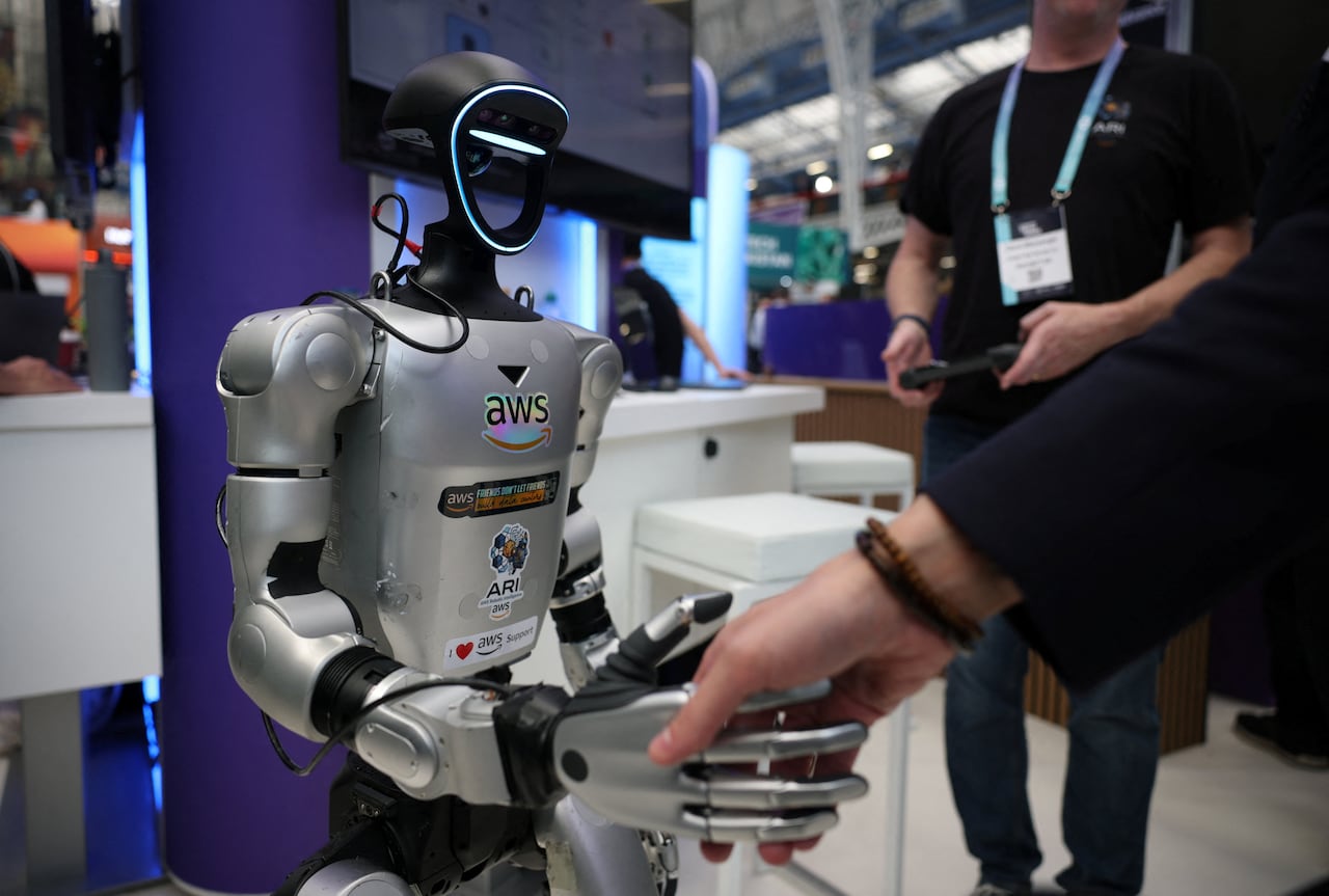 A silver robot shakes hands with a person.