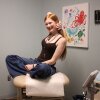 Veronica, 17, is a teen with long, straight red hair, wearing a camisole top, jeans and necklaces. She's sitting cross-legged on a medical exam table, smiling.