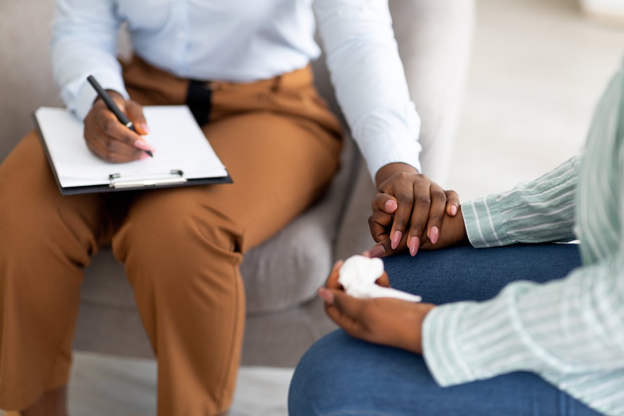 A Black woman doctor puts a hand on the hand of a Black woman patient.