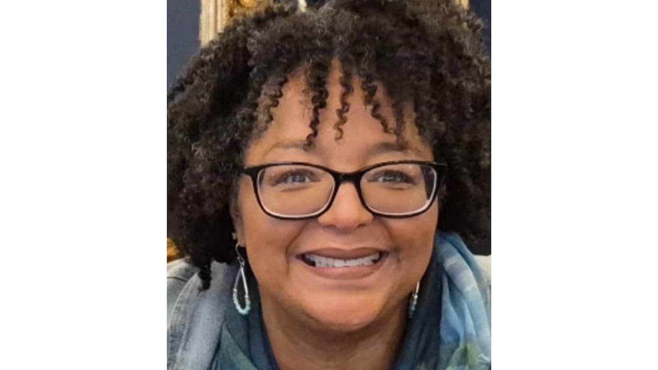 A Black woman wearing glasses smiles at the camera.