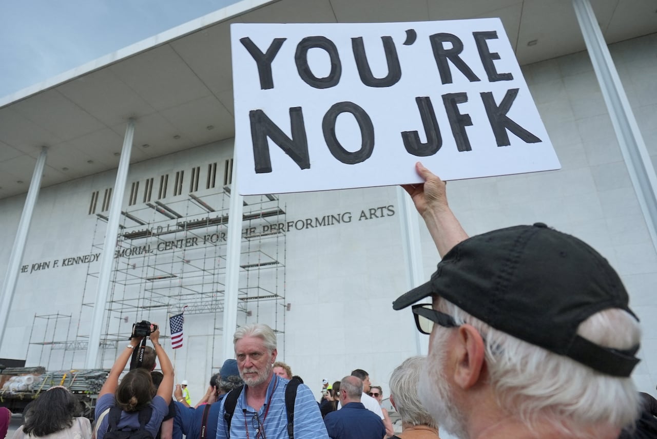 A man holding a sign reading 'You're No JFK' outside the Kennedy Center in Washington, D.C.