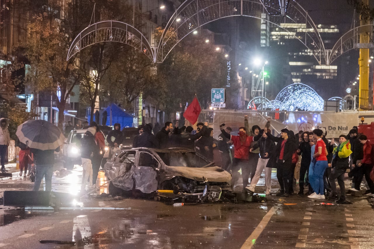 People cheer and hold signs next to a burned out car