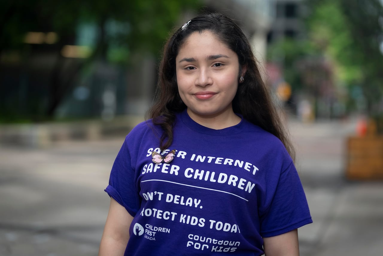 An outdoor portrait of smiling teen girl in a purple t-shirt with white letters reading "Safer internet, safer children."