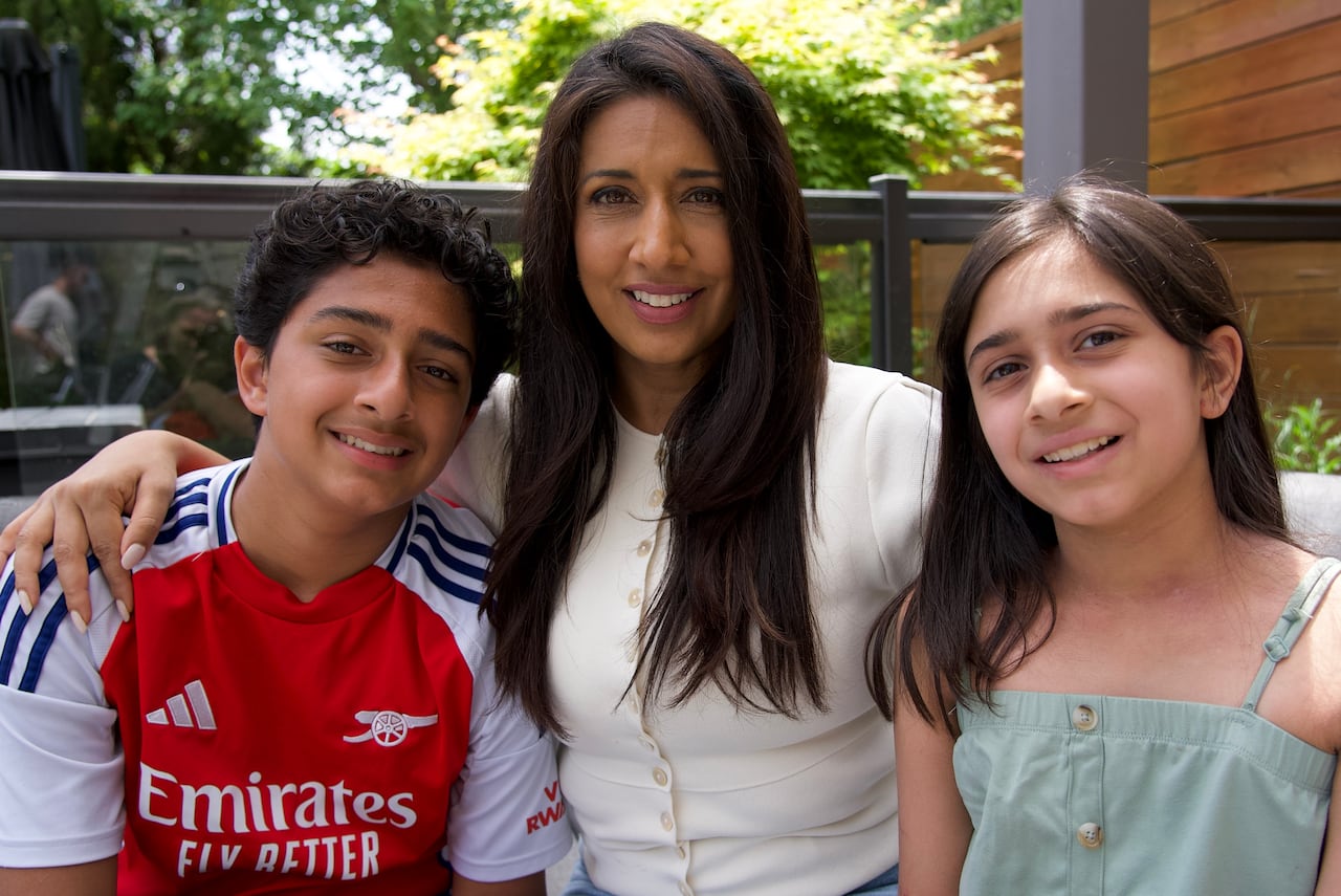 A portrait of a woman with long hair sitting between a boy in a red and white soccer jersey and a girl in a light green tank top.