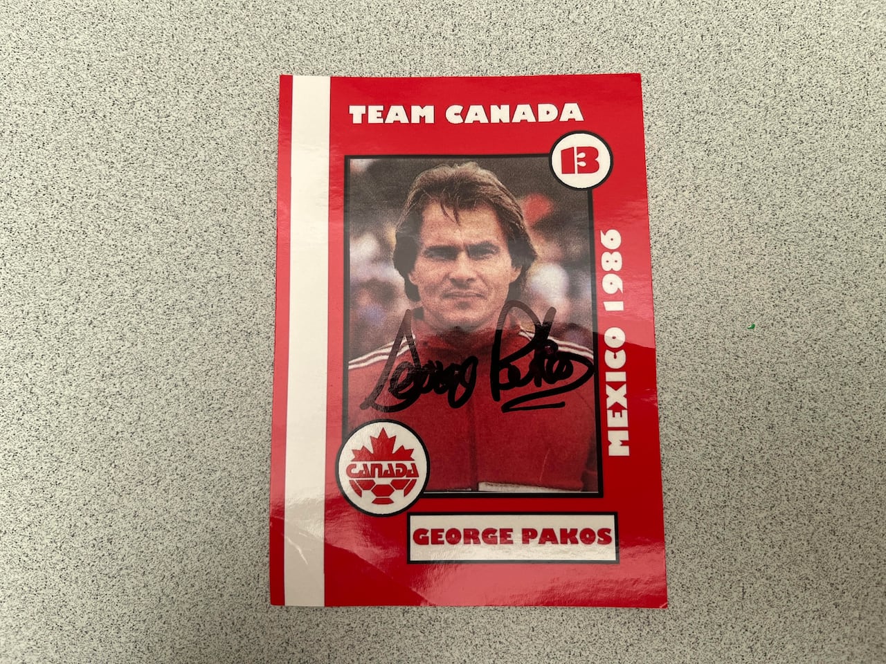 A red soccer card featuring George Pakos of Team Canada at the World Cup in 1986.