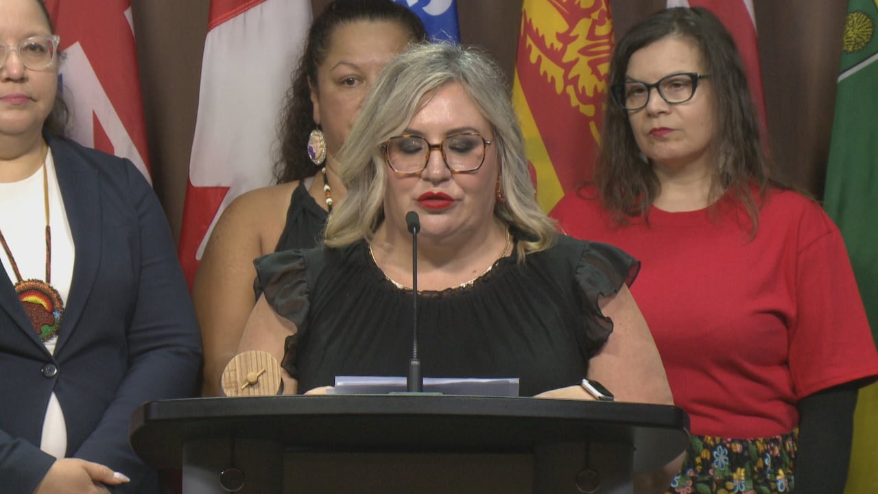 Close up of van Oirschot at the podium looking down at her notes while three women stand behind her.