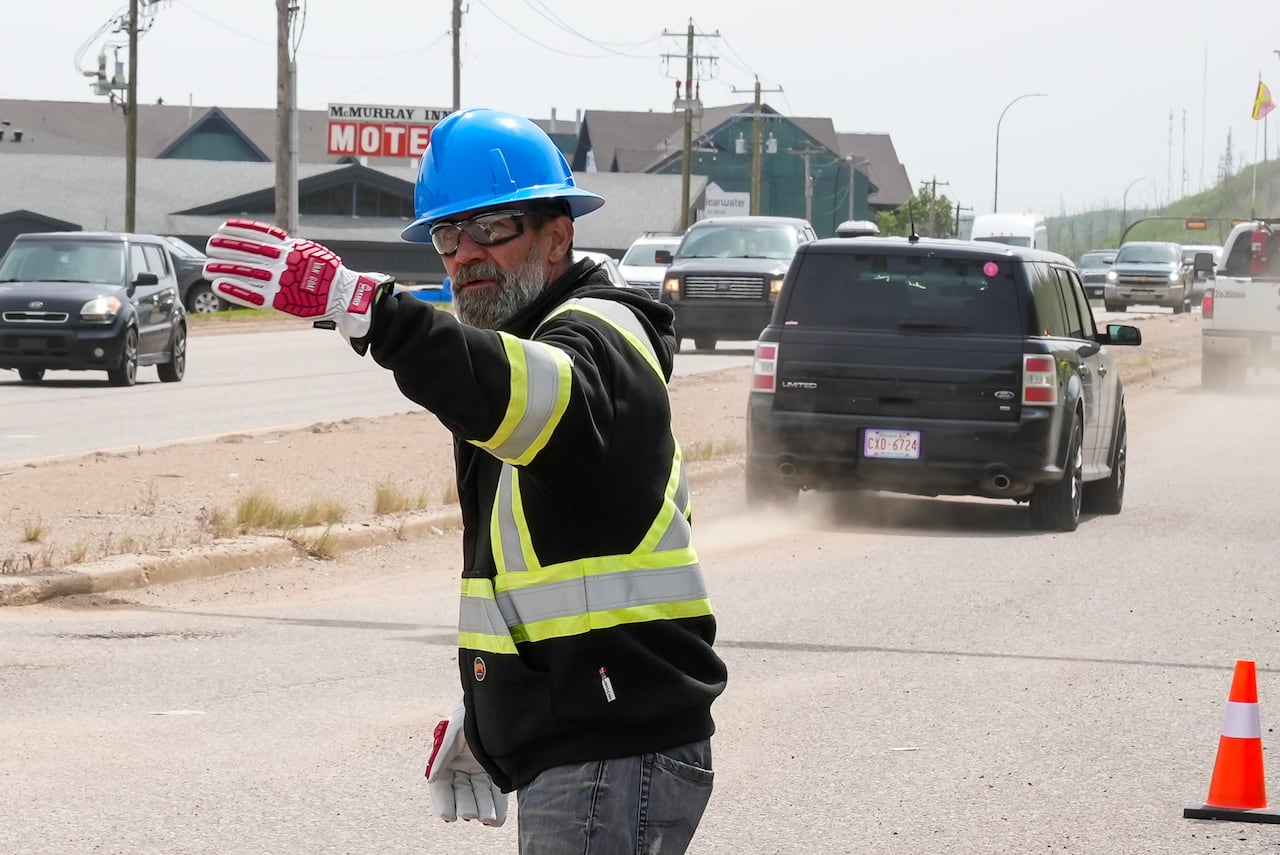 A man in a hard hat and safety vest directs traffic