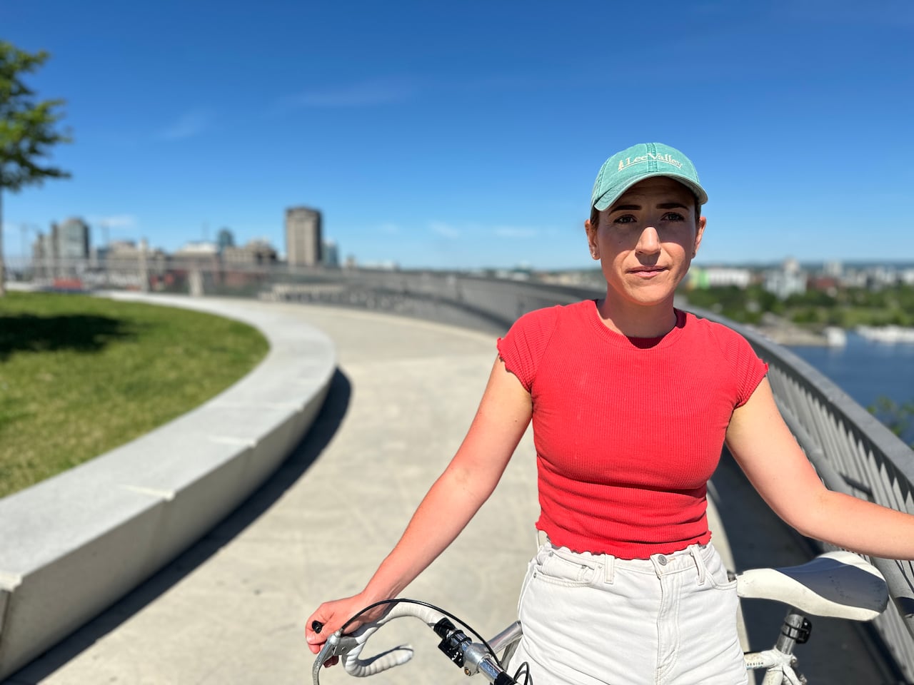 A woman stands with her bike on a pathway on a sunny summer day.