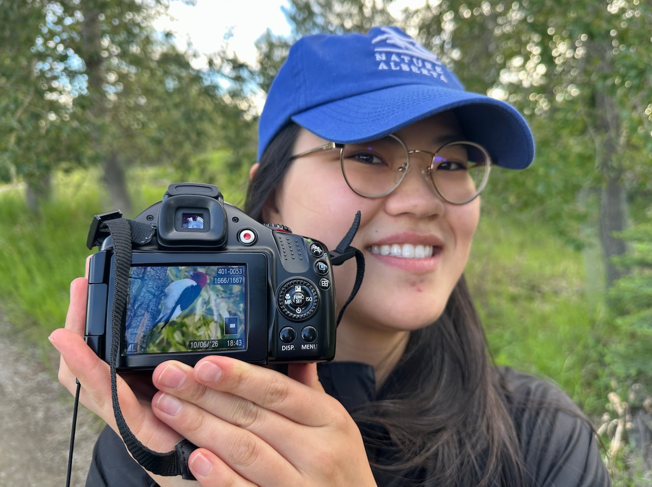 A woman holds up a camera with a picture of a woodpecker on it.