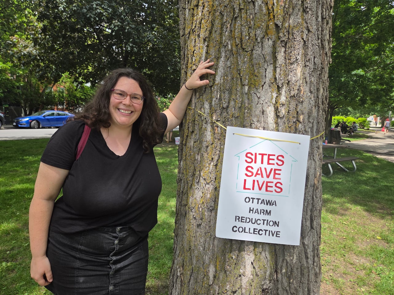 a woman in black leaning against a tree