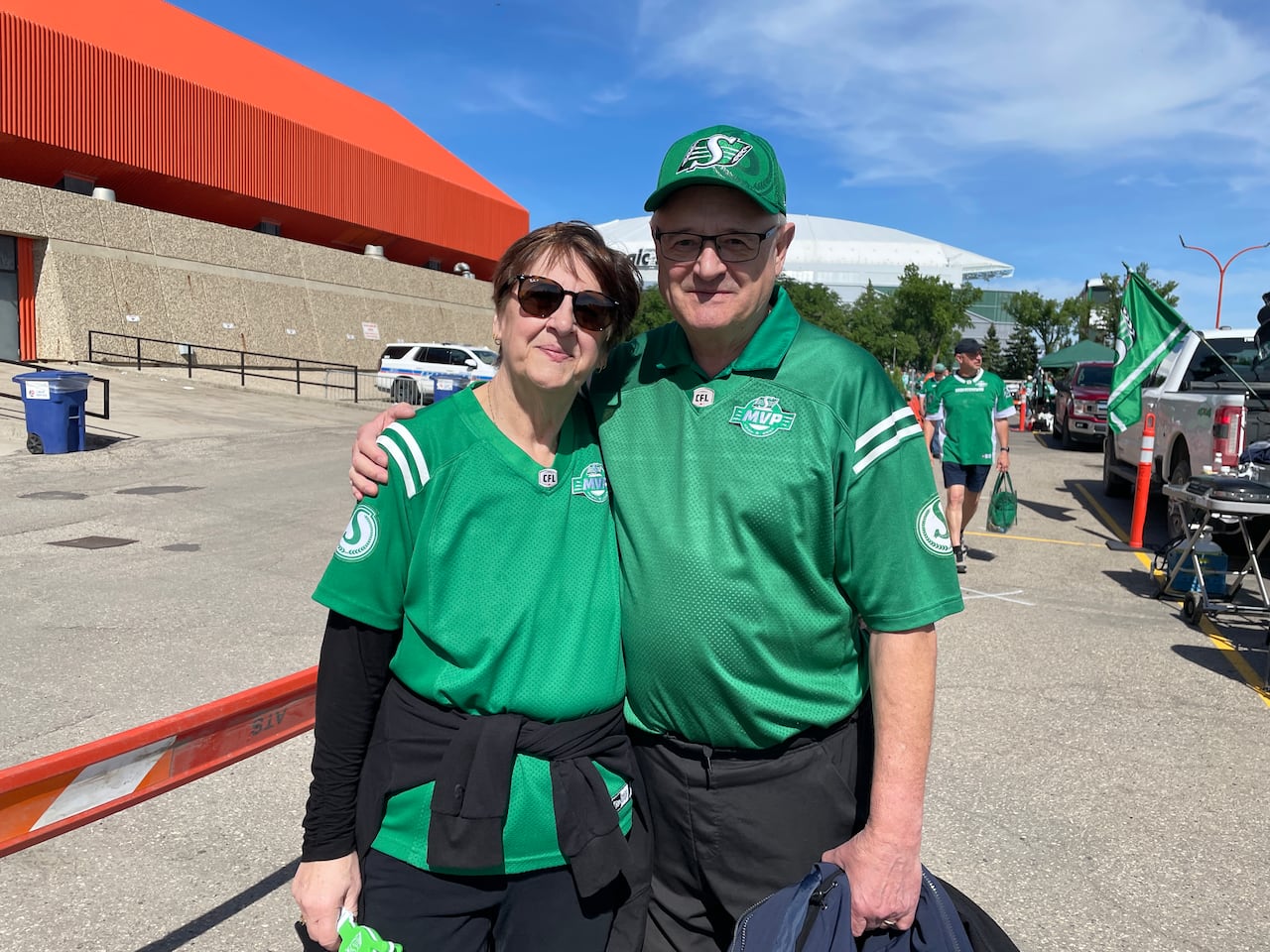 A man and woman wearing green Saskatchewan Roughrider jerseys stand next to each other.