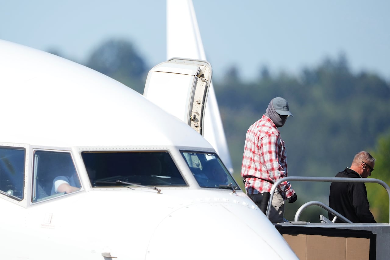 A worker in a mask walks off of a U.S. Immigration and Customs Enforcement flight departing from King County International Airport-Boeing Field, Saturday, Aug. 23, 2025, in Seattle. (AP Photo/Lindsey Wasson)