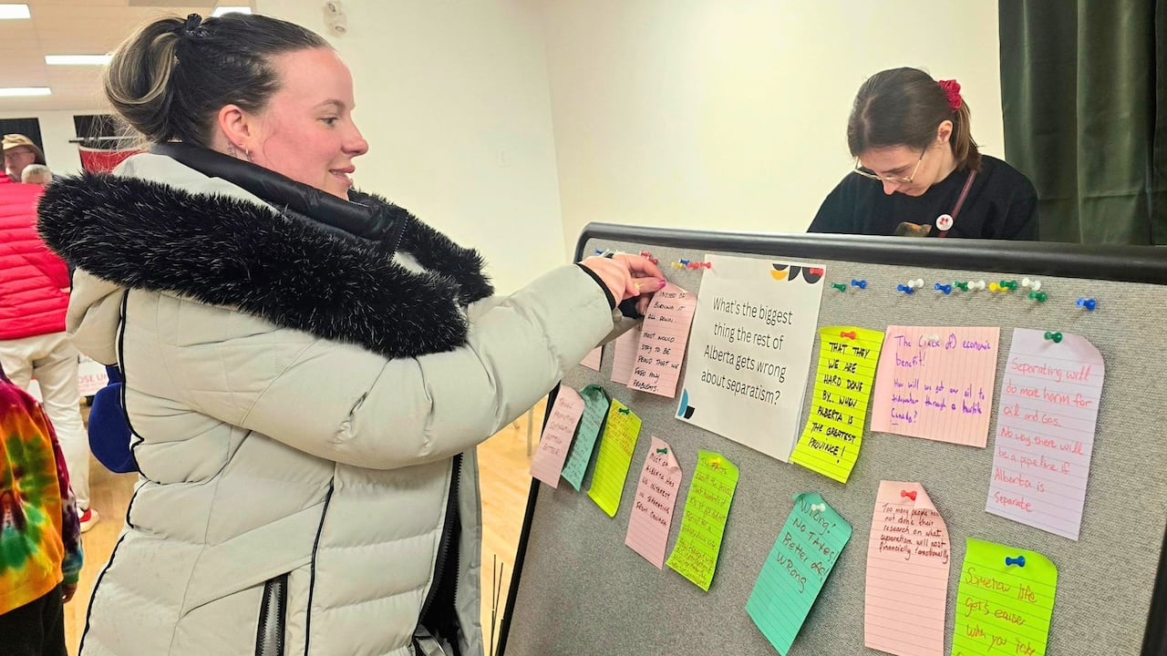 A woman pins a Post It note to a board with a question on it. The question reads: What's the biggest thing the rest of Alberta gets wrong about separatism?