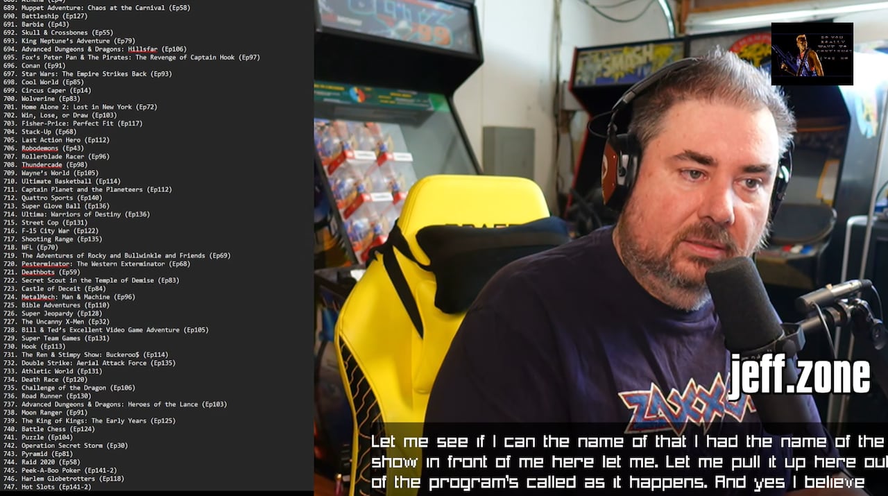 A man with brown hair sits in a garage full of video game paraphernalia. A running list of video game titles is seen, taken from a computer screen, on the left side.