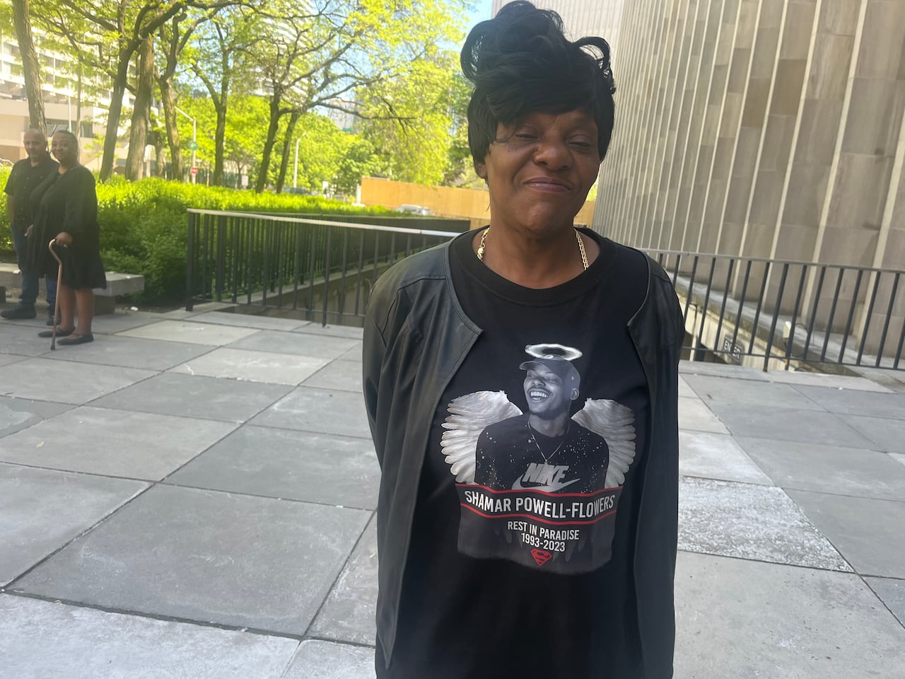 A woman stands outside wearing a shirt with her son's photo and angel wings around it.