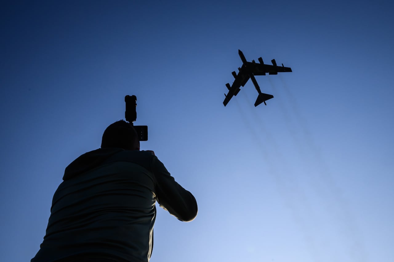 A B-52 in flight, seen from below, with a photographer looking up toward the aircraft and taking a photo.