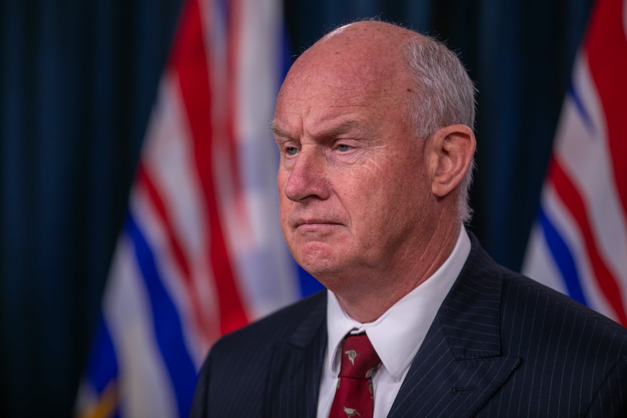 A man wearing a purple tie stands in front of B.C. flags.