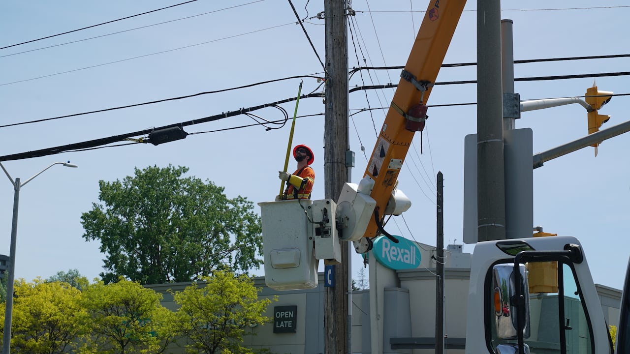A man wearing a reflective orange suit inside a lift uses a pole to adjust power lines