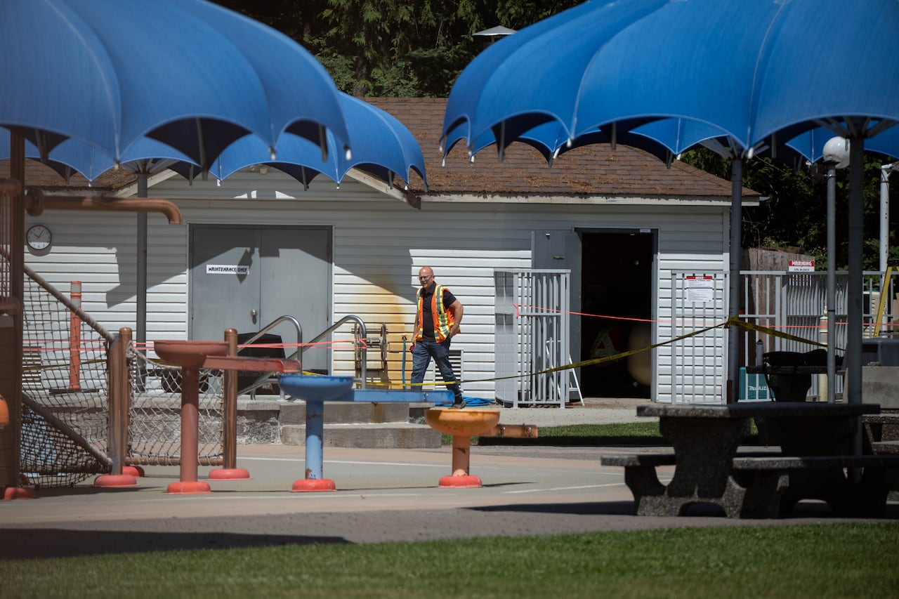 A man in an orange and yellow work vest walks behind caution tape with patio umbrellas in the foreground.
