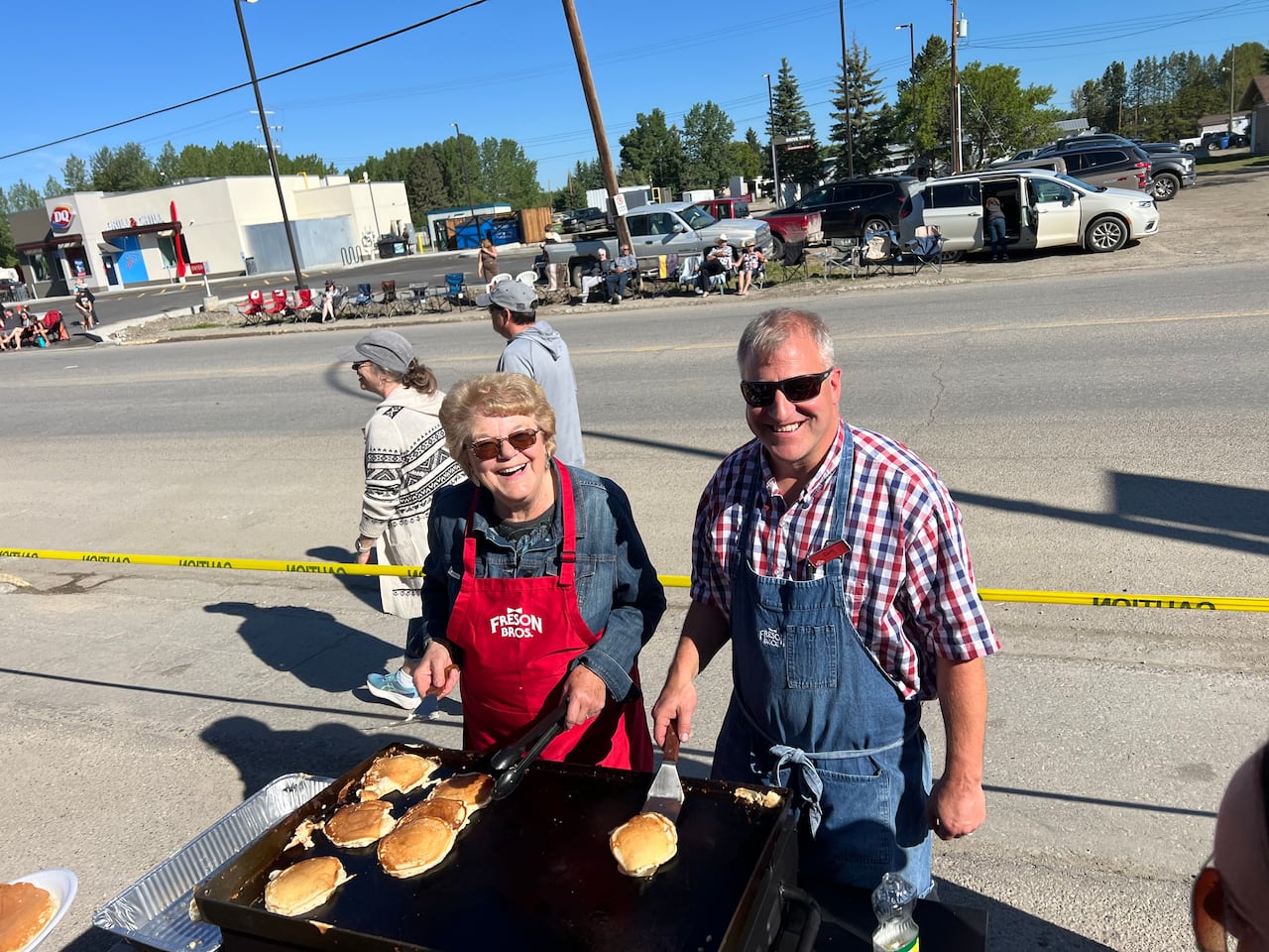 A woman and man flip pancakes on a griddle that is set up by the side of the road.