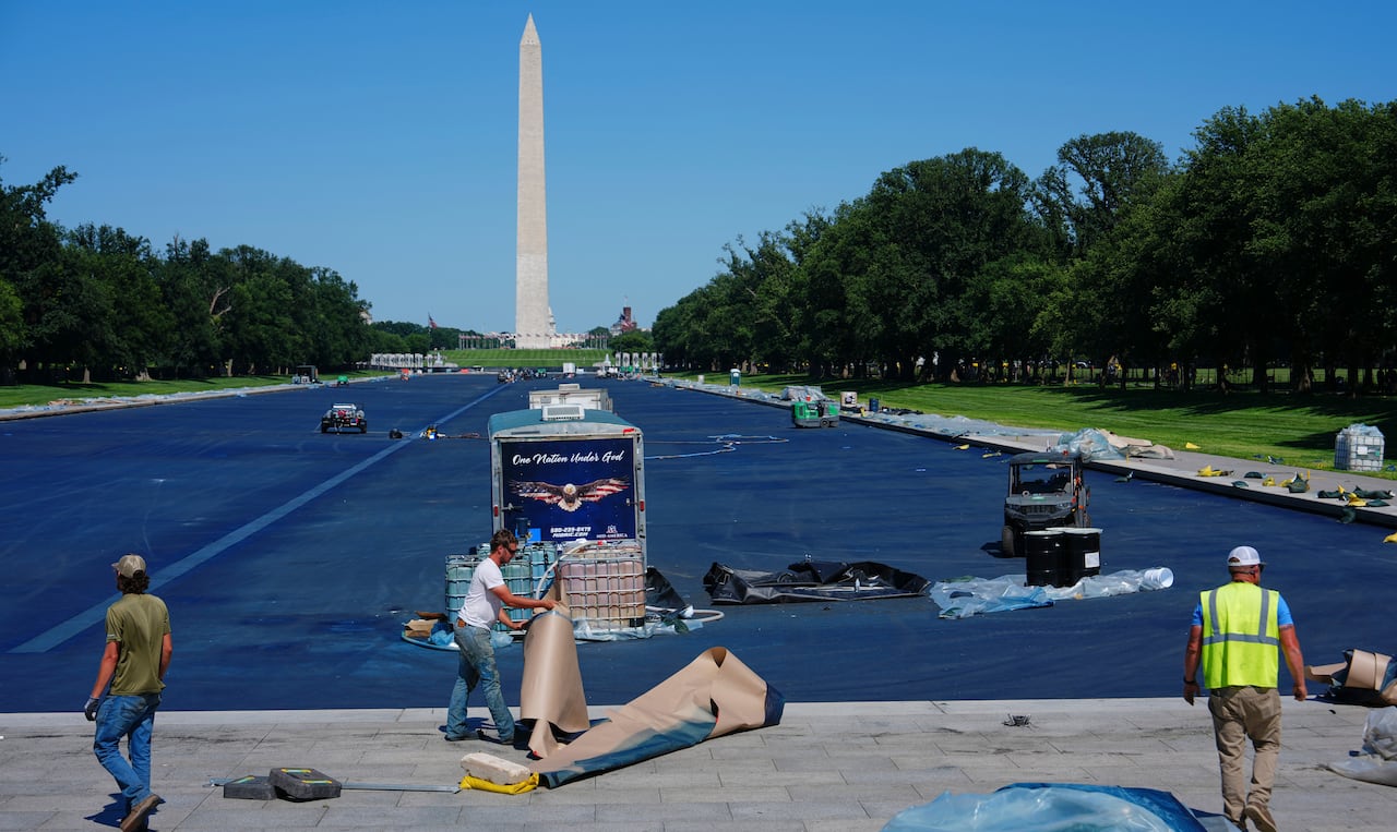 Workers are seen in front of the dark blue painted reflecting pool, with the Washington Monument in the background.