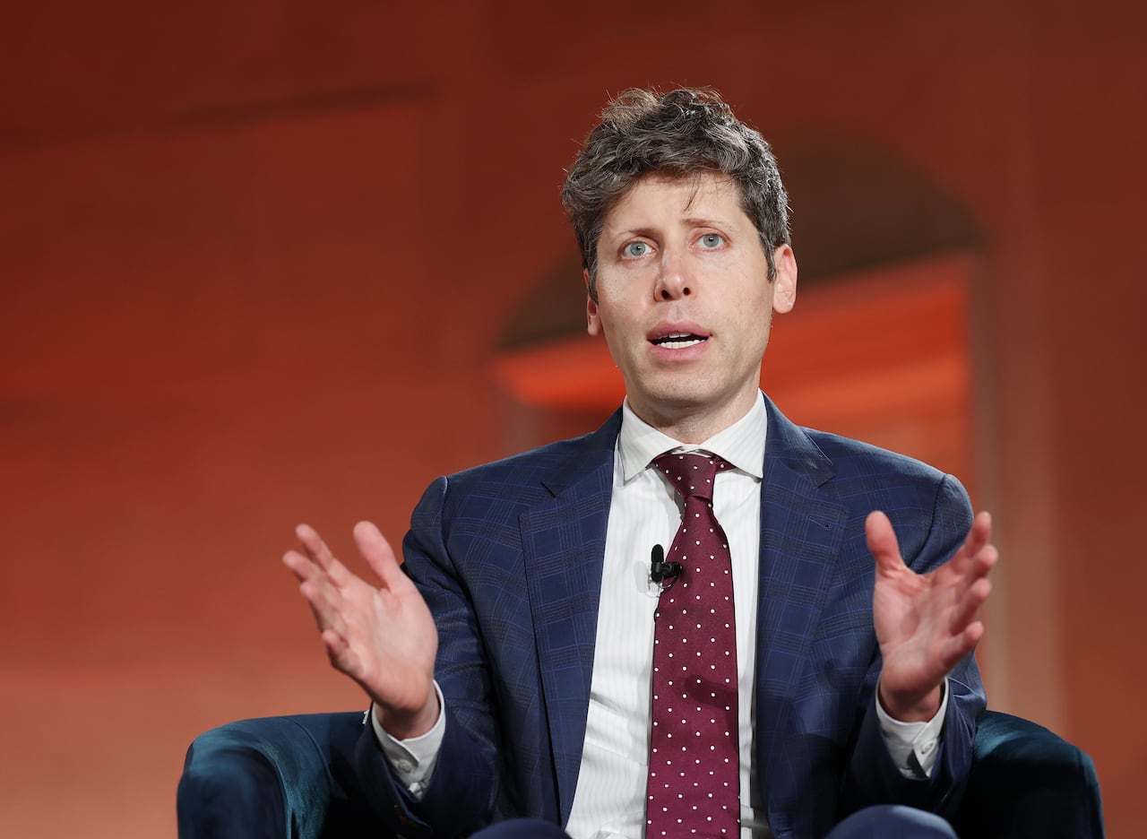 A man in a suit sits with his hands raised.