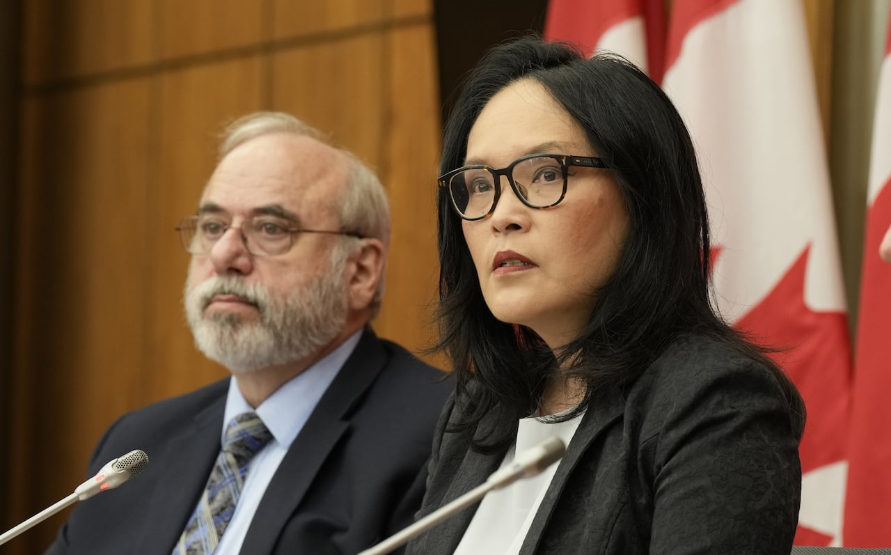 Two people are seen sitting behind microphones.