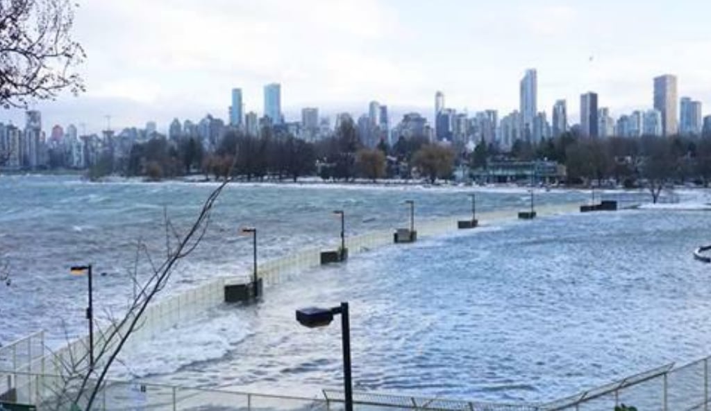 A king tide engulfs the Kitsilano Pool with the Vancouver cityscape in the background.