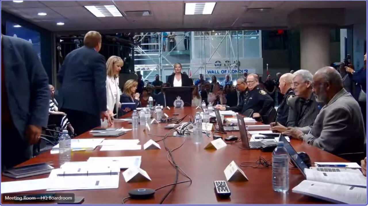 People are seen rising from a board table with multiple people visible in the background.