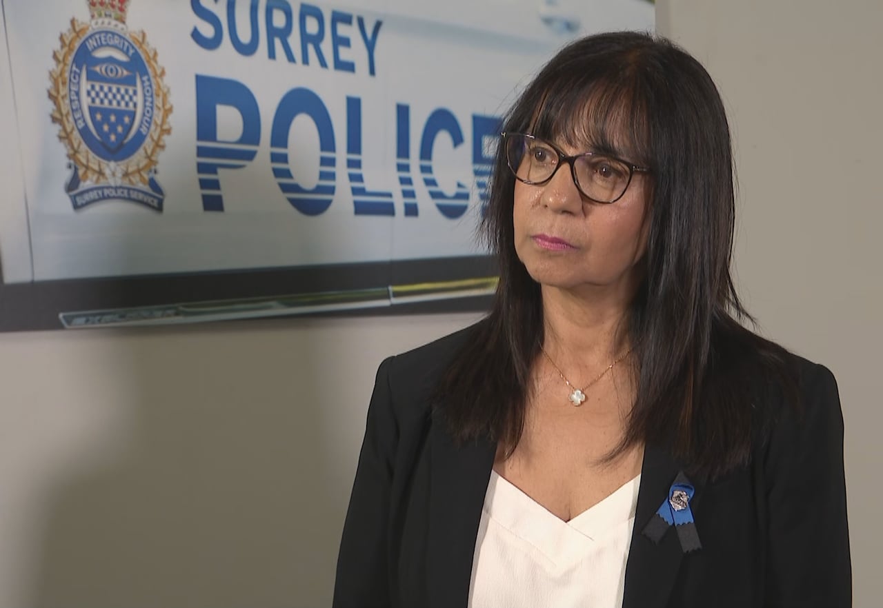 A South Asian woman is seen in front of a banner reading 'Surrey Police Service'.
