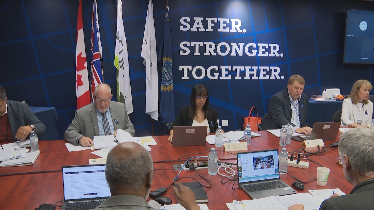 People sit at a board table and look through laptops and documents.
