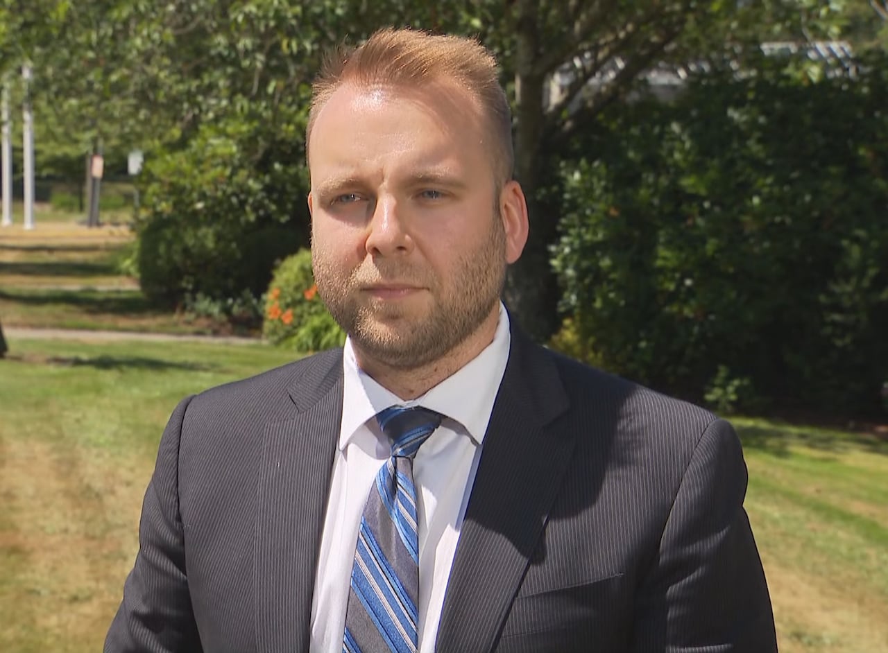 A white man wearing a suit is seen near a lawn on a sunny day.