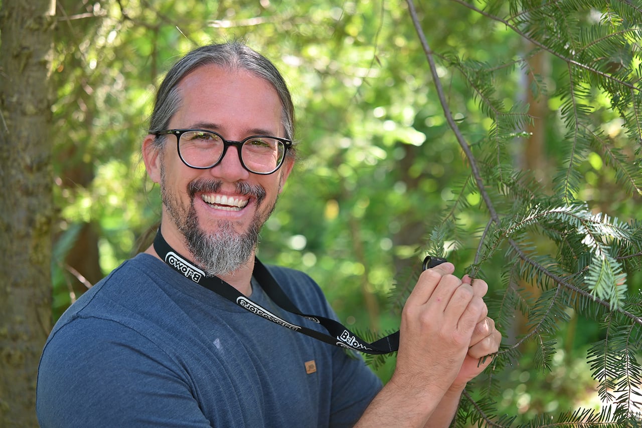 A man is holding a microscope and looking at a tree.