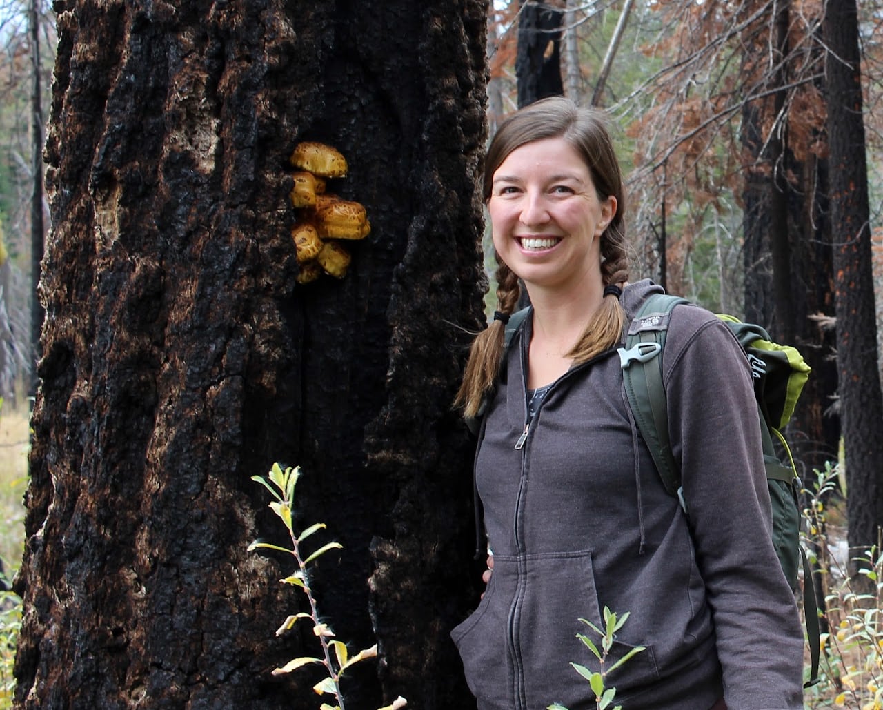 A woman is standing next to a tree covered in tiny orange mushrooms.