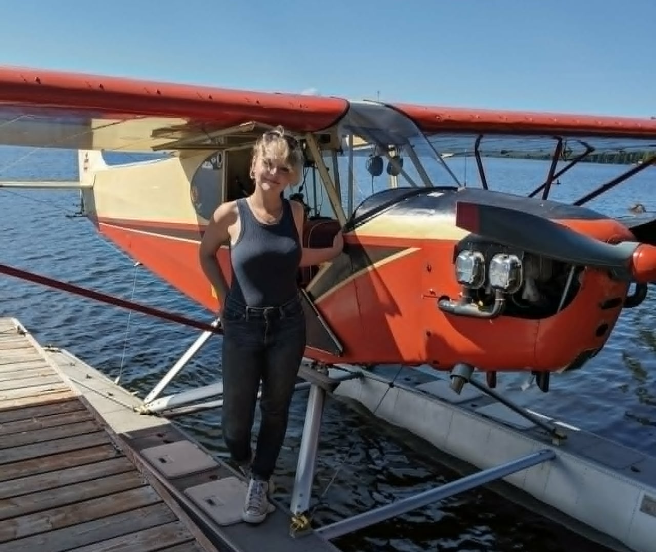 A young woman standing next to a float plane on a dock.