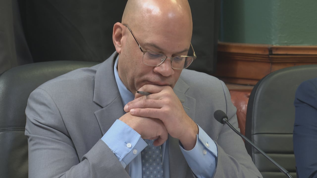 Man in glasses and grey suit looks down.