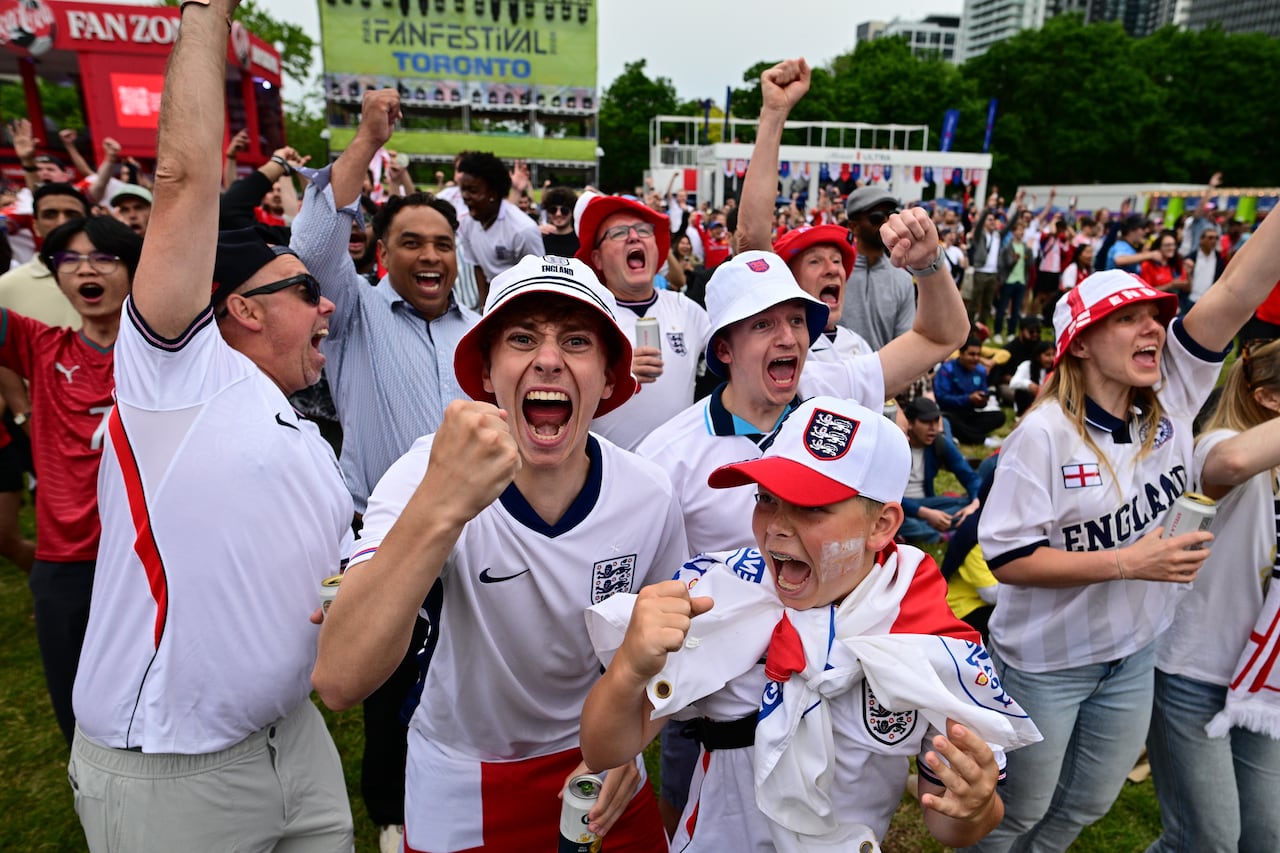 Fans in England's jerseys put their fists in the air and cheer for a goal.