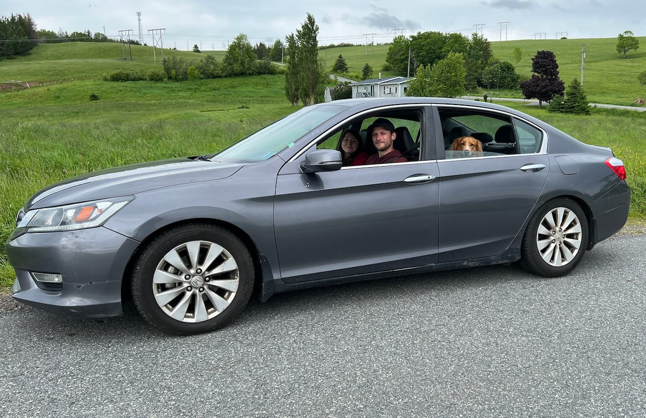 A man, woman and dog sitting in a grey car.