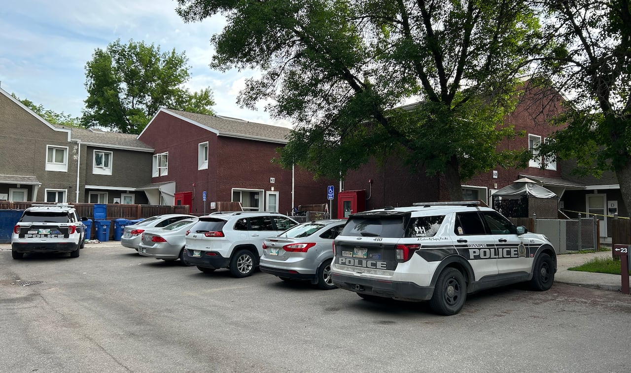 Two police cruisers parked outside a housing complex that has been taped off by investigators.