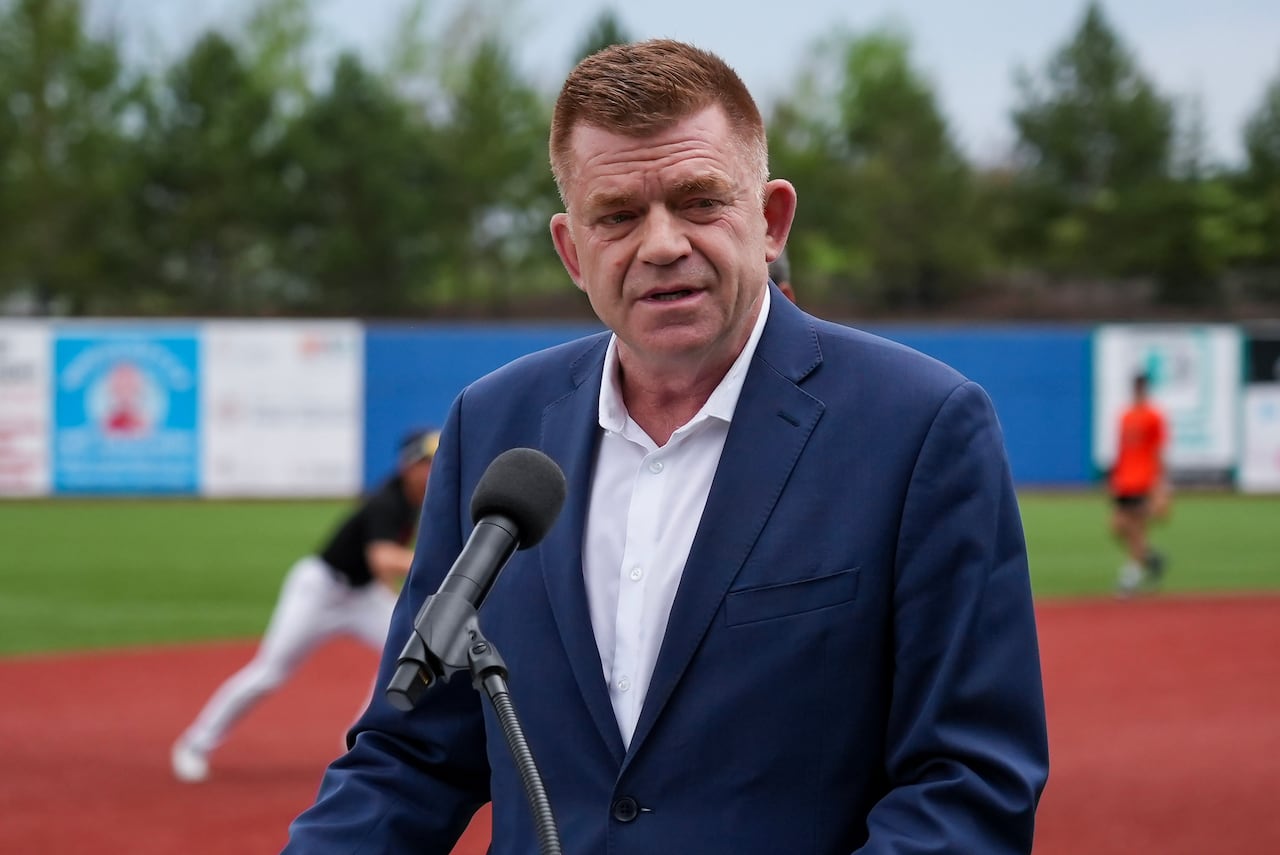 A man in a blue suit speaks at a podium in the middle of a baseball field.