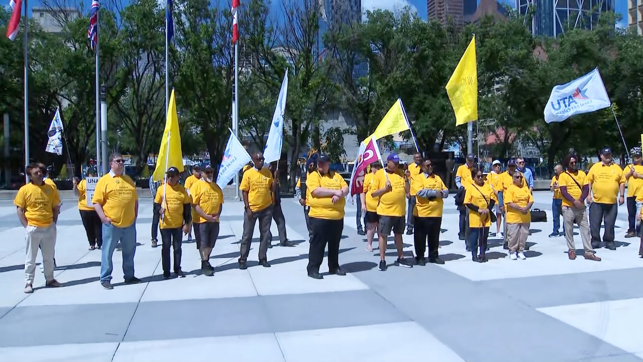 About two dozen people wearing yellow T-shirts and holding yellow flags assemble in a city square.
