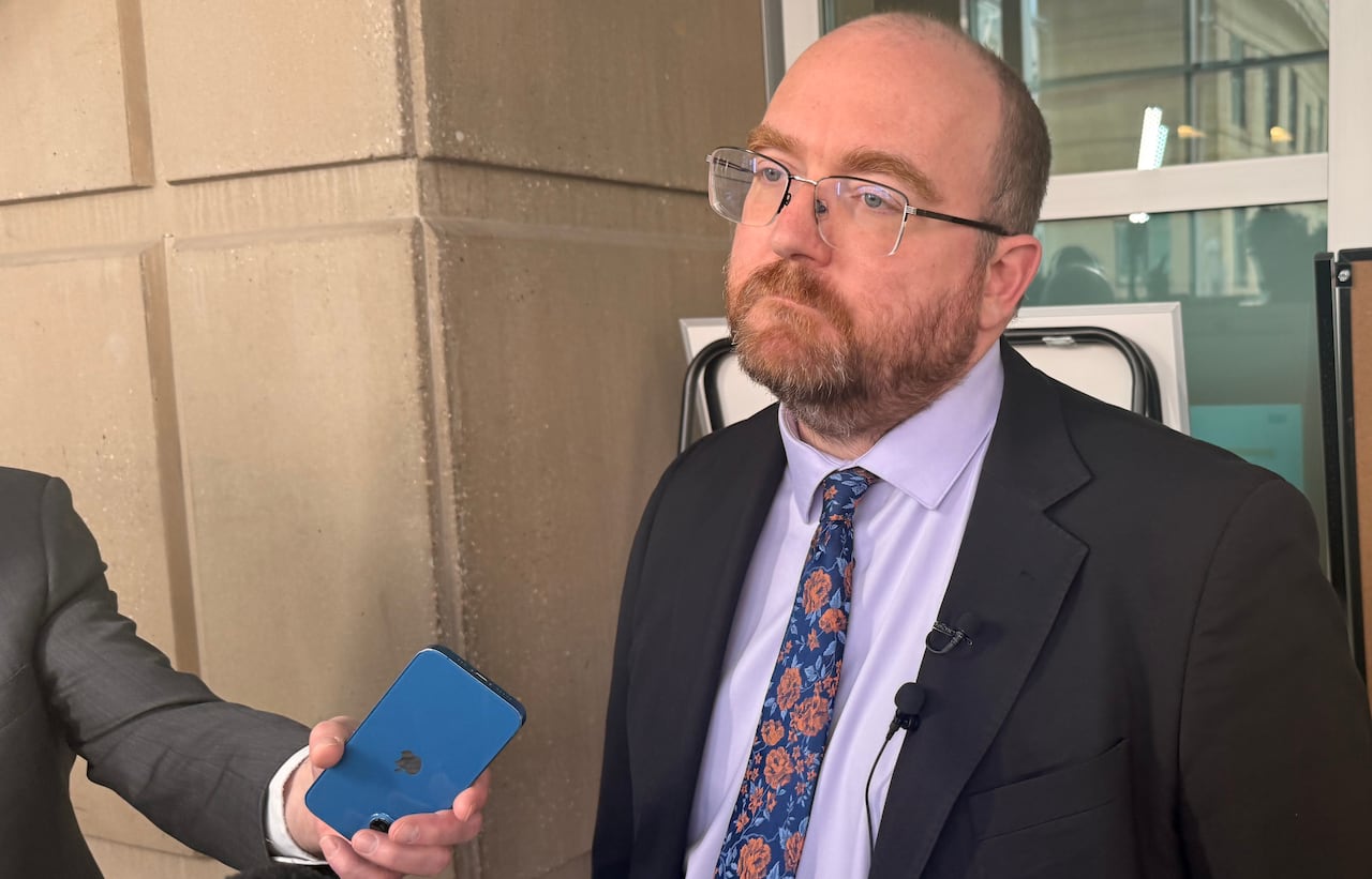 A man in a suit speaks with reporters.