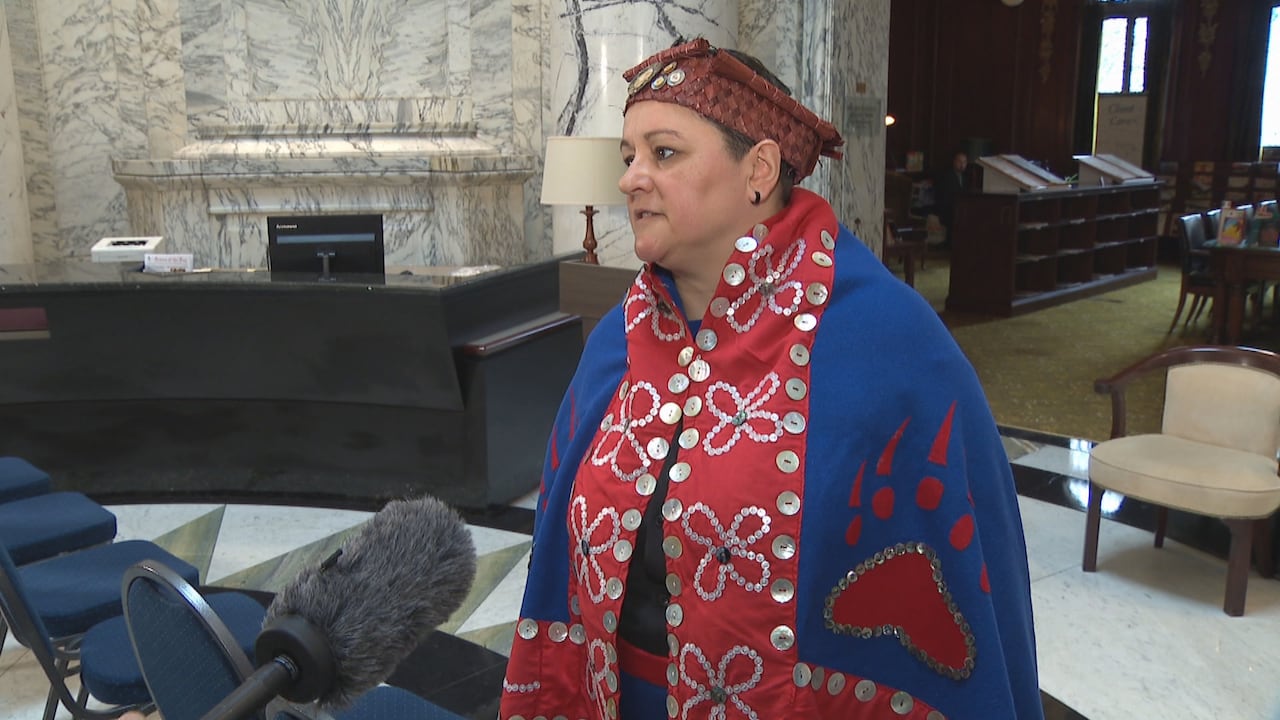 A woman wearing First Nations regalia talks to reporters in the B.C. Legislature.