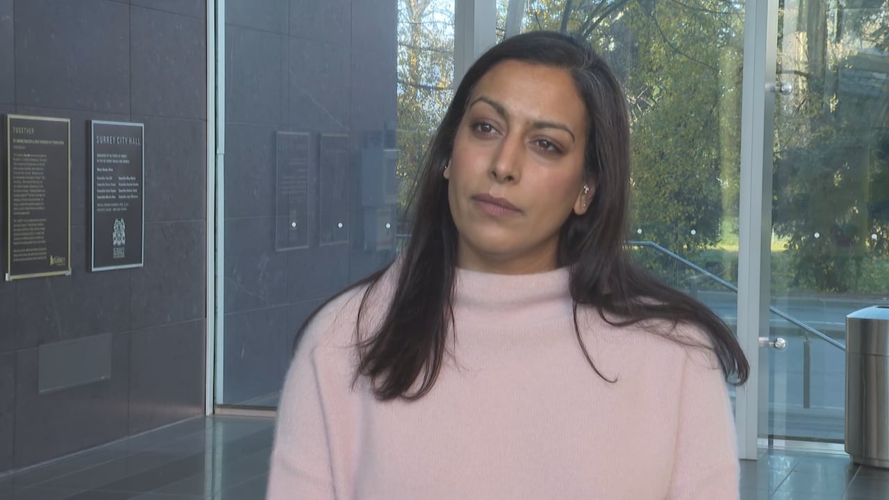 A South Asian woman wearing a pink sweater is seen outside a door.