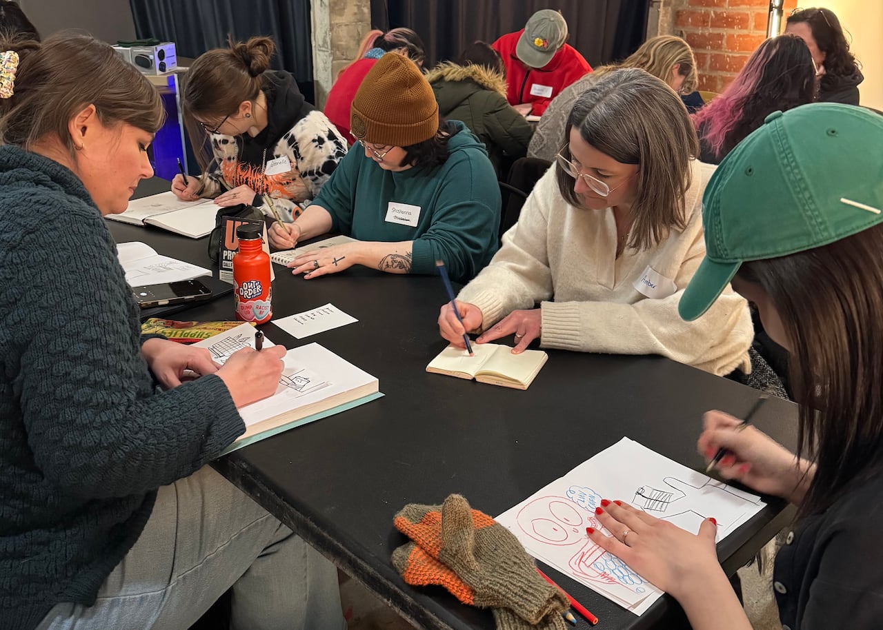 A group of people bend their heads over tables as they draw.