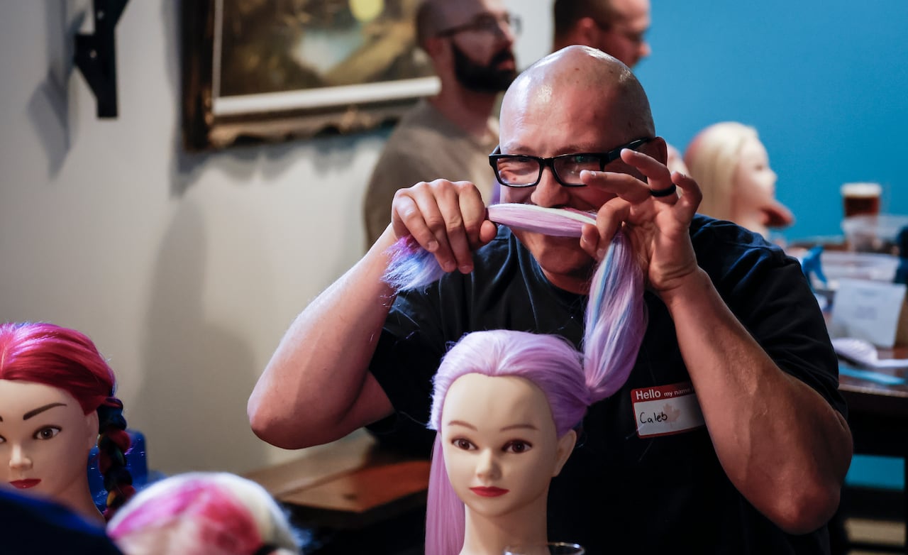 A bald man with glasses holds up a mannequin's pigtail in front of his face like a moustache