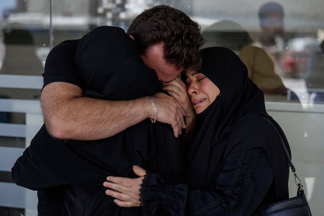 A man embraces two women who appear to be weeping.