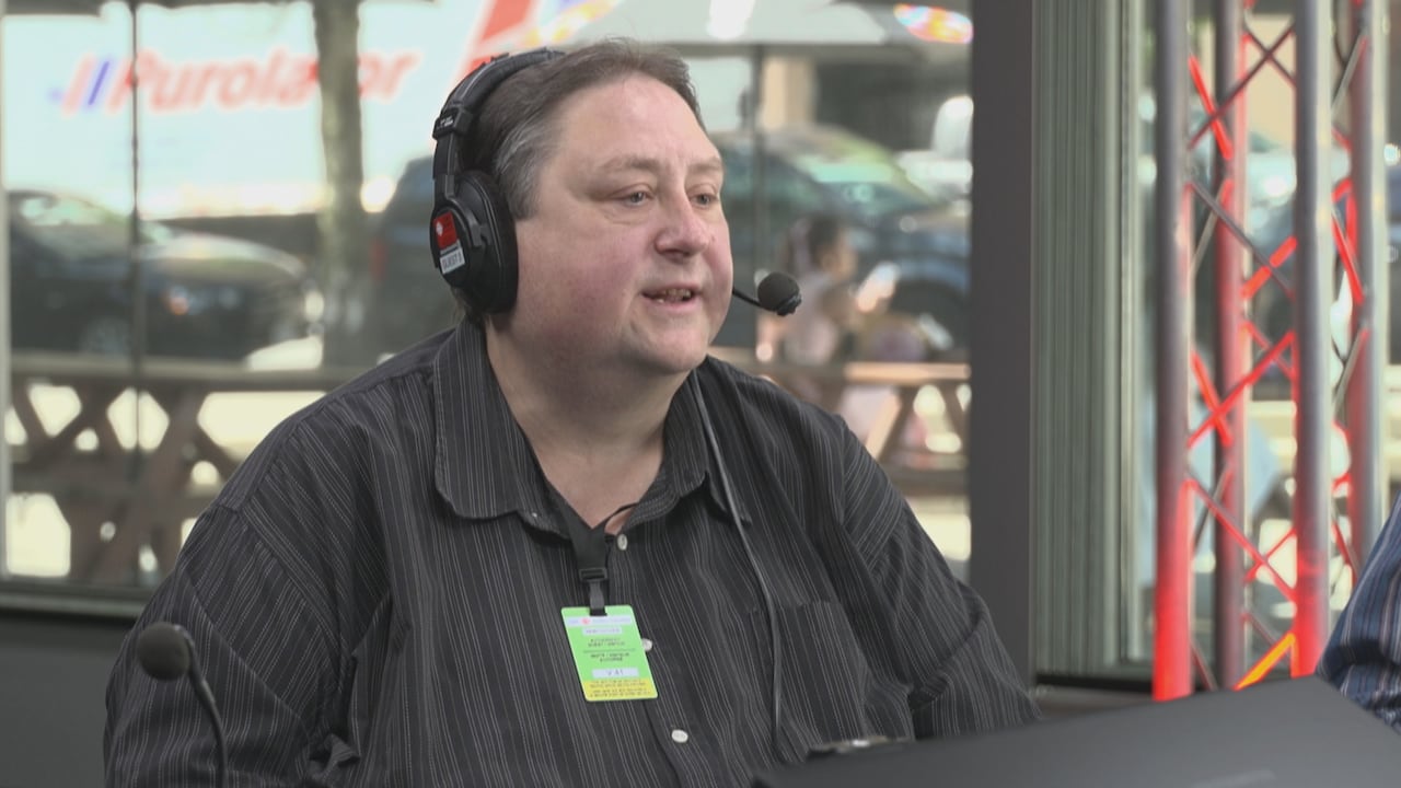 A man wearing a headset sitting at a desk with microphones on it during a radio interview