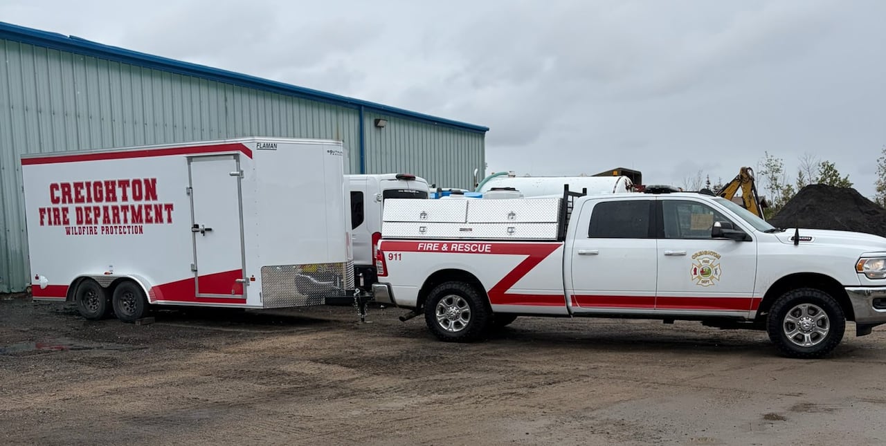 A white truck and trailer with red markings parked in a gravel area.